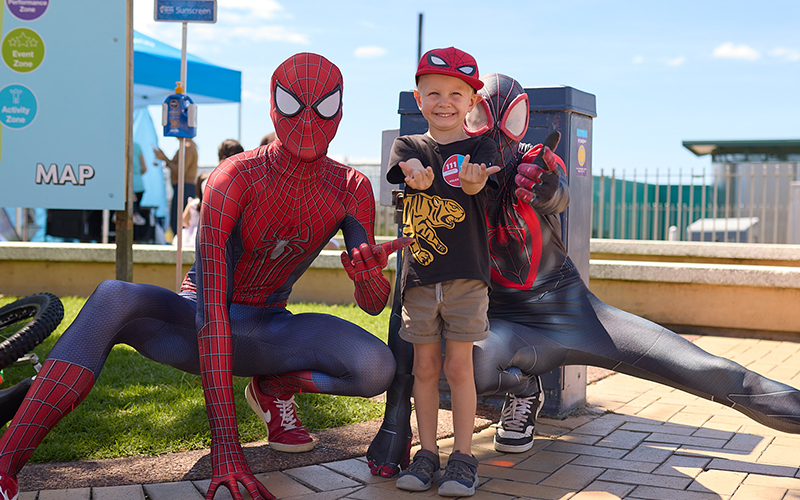 Boy standing with two people dressed as Spiderman characters